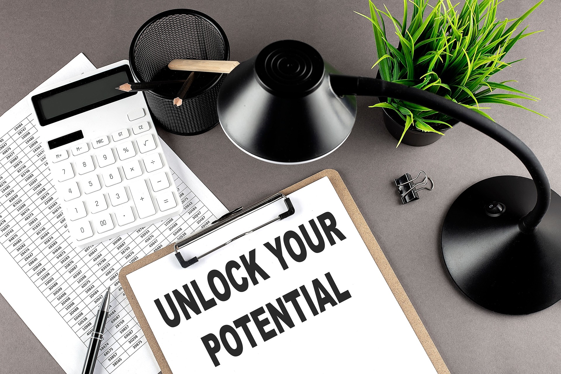 Clipboard ,chart and calculator, lamp and workspace accessories on a grey table. Top view , text UNLOCK YOUR POTENTIAL